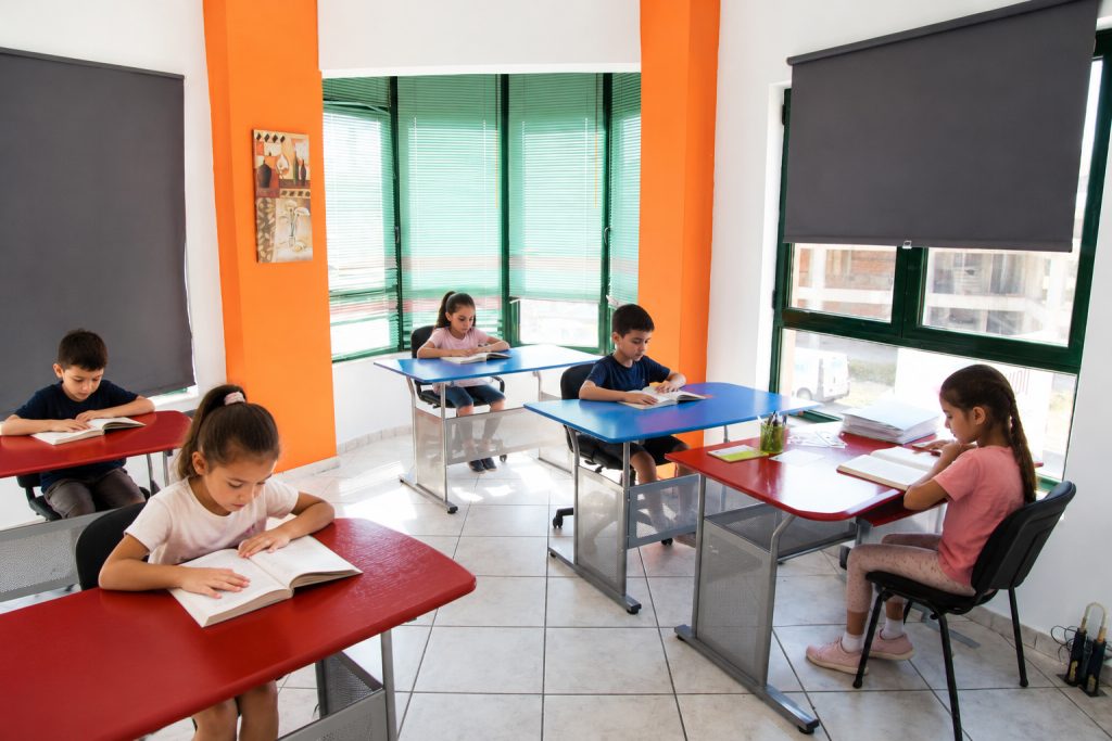 Φωτεινή αίθουσα διδασκαλίας με παιδιά δημοτικού που διαβάζουν ήσυχα σε θρανία.